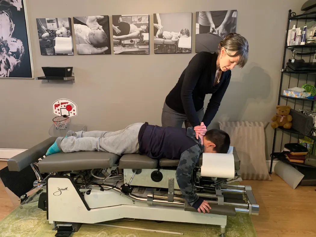 Dr. Emilie Perras adjusting neck of young boy laying face down on treatment table
